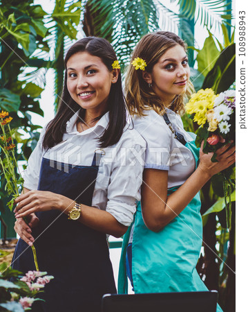 Half length portrait of successful gardeners dressed in casual aprons holding fresh flowers in hands 108988943