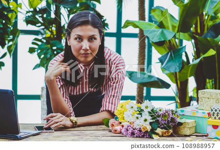 female florist spending time in orangery near desk with laptop 108988957