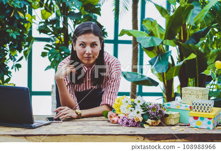 female florist spending time in orangery near desk with laptop 108988966