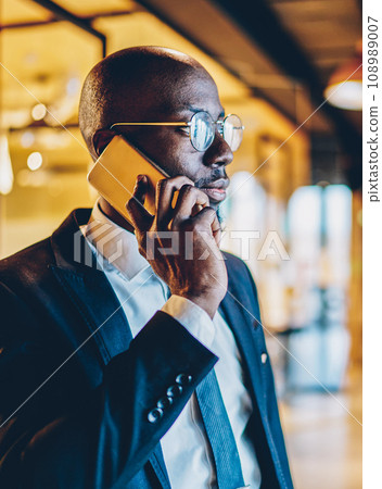 Experienced dark skinned proud ceo in black suit talking on telephone device 108989007