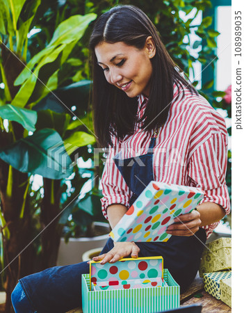 Positive asian woman in apron working in flower shop making decoration for presents Positive asian woman in apron working in flower shop making decoration for presents 108989035