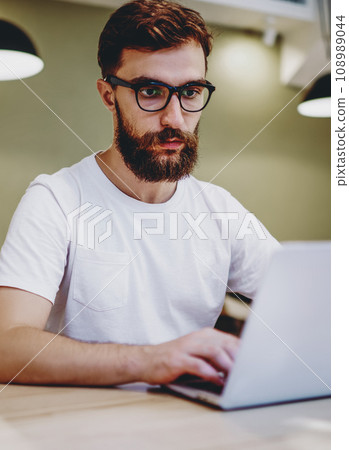 Serious male blogger in spectacles typing text of article for publication on laptop computer Serious male blogger in spectacles typing text of article for publication on laptop computer 108989044
