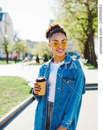 positive woman in trendy apparel looking at camera while holding cup with takeaway coffee positive woman in trendy apparel looking at camera while holding cup with takeaway coffee 108989061