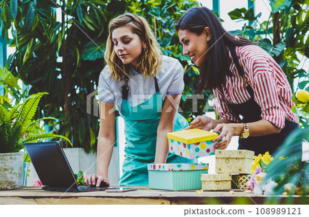 Positive successful female florists searching addresses of clients via application on modern laptop computer 108989121