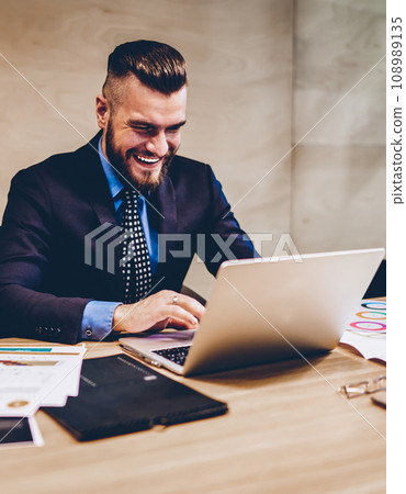 Successful entrepreneur in suit laughing during video call on laptop in office 108989135