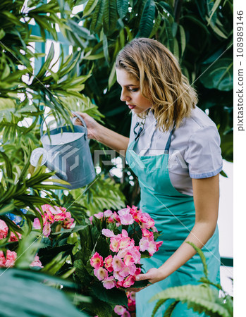 Professional female employee of orangery watering flowers with can and taking care of plants Professional female employee of orangery watering flowers with can and taking care of plants 108989146
