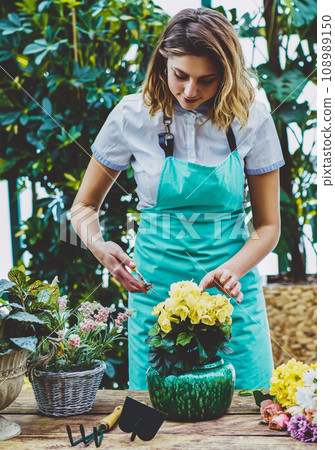 Positive female florist in apron taking care about flowers Positive female florist in apron taking care about flowers 108989150