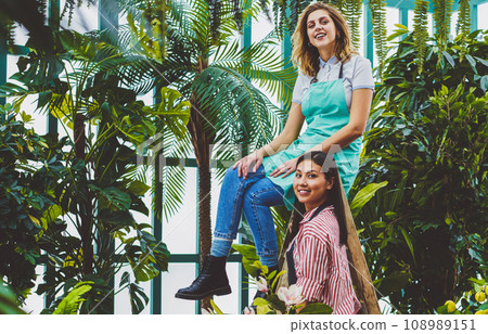 Portrait of cheerful excited female florists cooperating in glasshouse taking care about plants 108989151