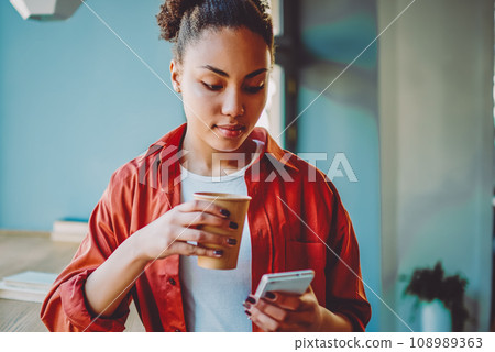 african woman holding paper cup with coffee and reading political news on website african woman holding paper cup with coffee and reading political news on website 108989363