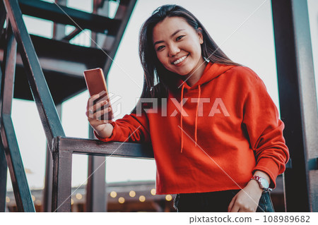 happy woman in stylish red hoody smiling at camera during leisure for chatting 108989682