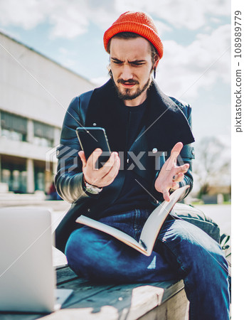 puzzled male student checking notification on cellular phone during e learning in campus 108989779