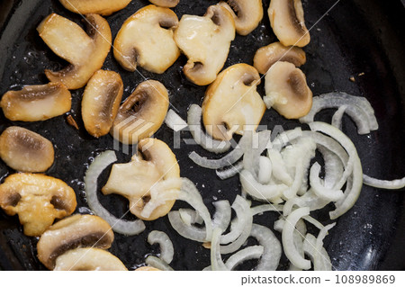Fried sliced champignons with onions in a pan. Mushrooms with onions in a pan. Cooking lunch and dinner. Fried onion rings. Fried sliced champignons with onions in a pan. Mushrooms with onions in a pan. Cooking lunch and dinner. Fried onion rings. 108989869