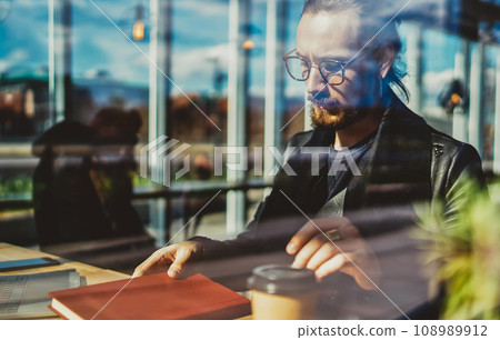 young hipster guy in trendy eyeglasses studying indoors with literature book young hipster guy in trendy eyeglasses studying indoors with literature book 108989912