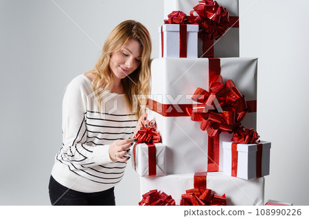 Beautiful woman poses among a mountain of white gift boxes in a gray background. 108990226