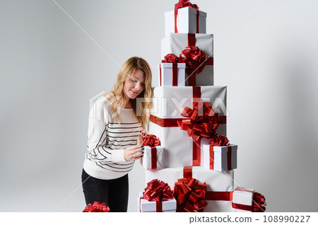 Beautiful woman poses among a mountain of white gift boxes in a gray background. 108990227