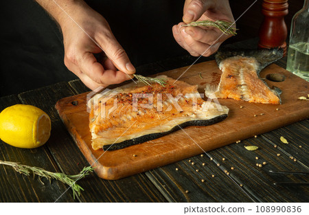 Adding rosemary to fish steaks for aroma and taste. Asian cuisine. The process of preparing fish by the hands of a chef in a restaurant kitchen Adding rosemary to fish steaks for aroma and taste. Asian cuisine. The process of preparing fish by the hands of a chef in a restaurant kitchen 108990836