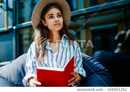 ,pensive hipster girl sitting outdoors with book looking up 108991262