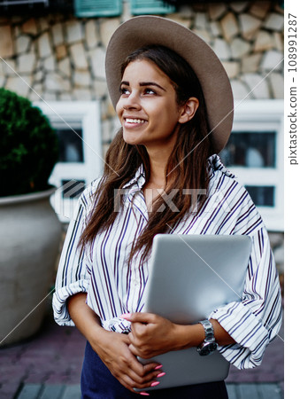 Smiling woman in trendy hat looking away satisfied with free time at street 108991287