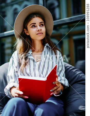pensive hipster girl sitting outdoors with book looking up pensive hipster girl sitting outdoors with book looking up 108991288