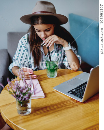 Pensive hipster girl drinking cocktail at cafeteria checking notification on mobile phone 108991307