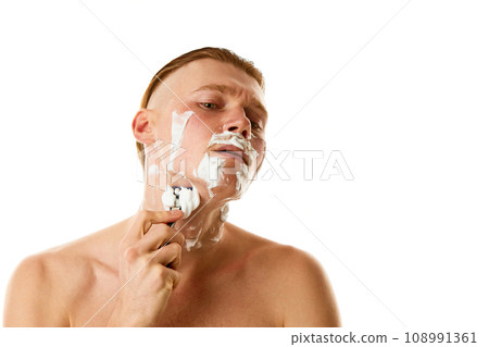Hygiene treatments. Attractive man shaving beard with shaving foam looking at camera against white studio background. Hygiene treatments. Attractive man shaving beard with shaving foam looking at camera against white studio background. 108991361
