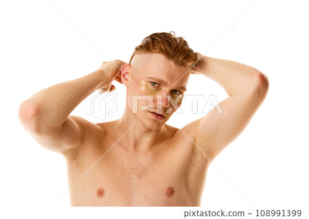 Young man styles, combing hair looking at camera with hydrogel patches under eyes against white studio background. 108991399