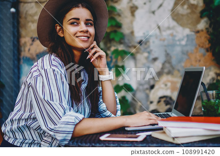 Young hipster girl sitting with laptop computer at cafe on street satisfied with idea for blog 108991420