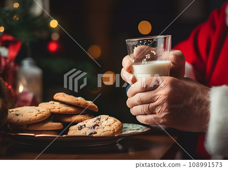 Close-up view of served glass of milk, freshly baked Christmas chocolate gingerbread cookies on wooden table for Santa Claus at home in front of new year fir tree lights. Santa having delicious snack 108991573