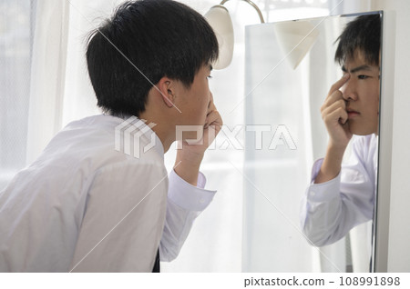 A middle school boy worries about his nose in the mirror at home 108991898
