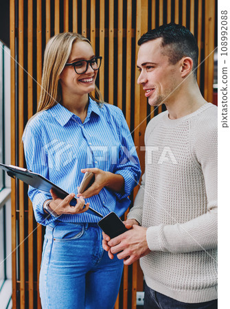 Cheerful young man and woman communicating with each other standing near window 108992088