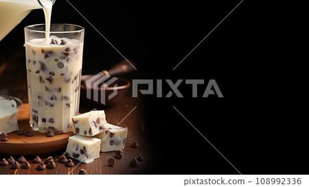 The milk is poured into a glass of chocolate chips. Milk dessert on a black background. 108992336