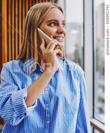 .Positive hipster girl laughing while calling on modern cellullar in office interior 108992391