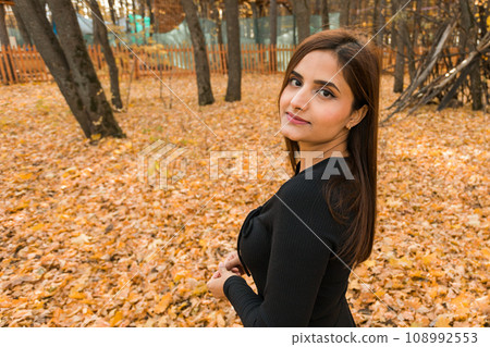 Close-up portrait of diversity young beautiful confident Indian Asian woman in black dress in fall outdoor copy space mockup. Happy and natural smiling female. Generation z and gen z youth concept 108992553