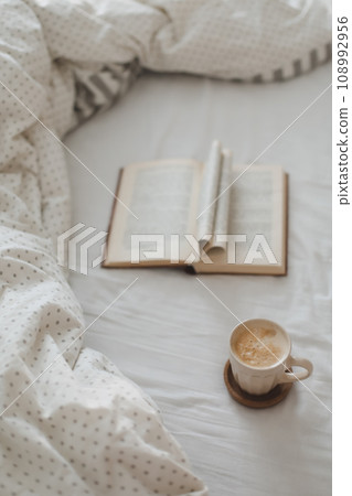 Cozy morning composition with a coffee cup and a book with pages folded into a heart shape in bed Cozy morning composition with a coffee cup and a book with pages folded into a heart shape in bed 108992956