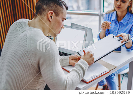 Young woman giving paper document for signing colleague during working process in office interior Young woman giving paper document for signing colleague during working process in office interior 108992989