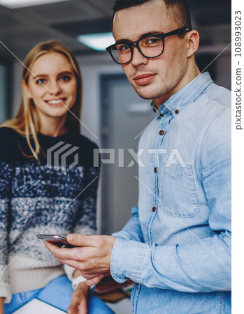 Two hipster students standing in coworking space.Young man with cellular in hand Two hipster students standing in coworking space.Young man with cellular in hand 108993023