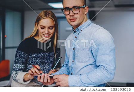 Portrait of good looking young man dressed in denim shirt looking at camera while positive female Portrait of good looking young man dressed in denim shirt looking at camera while positive female 108993036