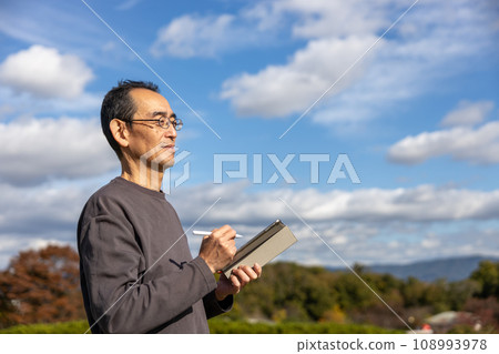 Mature man standing outdoors with a tablet 108993978