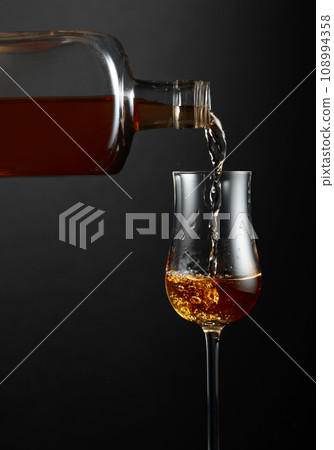 Strong alcohol drink is poured from a bottle into a glass. Strong alcohol drink is poured from a bottle into a glass. 108994358