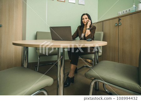 Smiling businesswoman using her phone in the office. Small business entrepreneur talking on mobile phone and smiling while communicating with her office 108994432