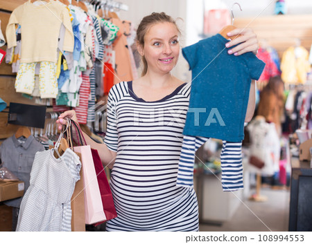 Pregnant woman in striped tunic chooses clothes for boy 108994553