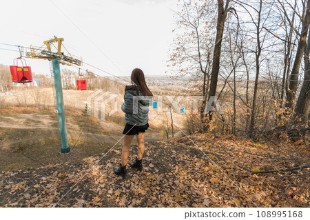Girl in fall park against background of cable car copy space. Woman with long curly hair. Beautiful sunlight in the forest. Hair care. Generation Z gen z and youth. Girl in fall park against background of cable car copy space. Woman with long curly hair. Beautiful sunlight in the forest. Hair care. Generation Z gen z and youth. 108995168