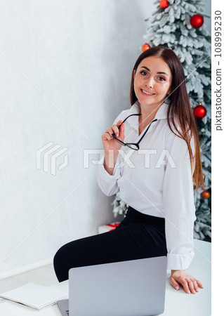 Young happy spanish businesswoman using smartphone while working laptop at home on Christmas 108995230
