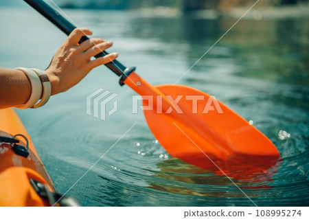 Kayak paddle sea vacation. Person paddles with orange paddle oar on kayak in sea. Leisure active lifestyle recreation activity rest tourism travel 108995274
