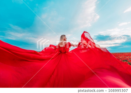 Woman poppy field red dress. Happy woman in a long red dress in a beautiful large poppy field. Blond stands with her back posing on a large field of red poppies 108995307