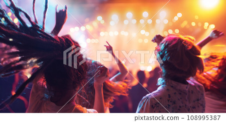 Crowd of expressive young people dancing raising hands and singing on tribunes on concert of favorite musical group in neon light. Crowd of expressive young people dancing raising hands and singing on tribunes on concert of favorite musical group in neon light. 108995387