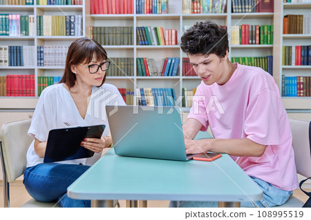 Female college counselor talking with young male student, meeting in library Female college counselor talking with young male student, meeting in library 108995519