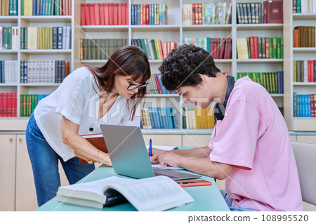 Woman mentor teaching male student in college library, exam preparation 108995520