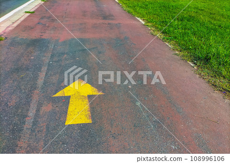 A yellow arrow drawn on the asphalt of a lane guiding pedestrians, cyclists and other road users. Traffic, mass, passenger flow management. A path that passes through various places and routes 108996106