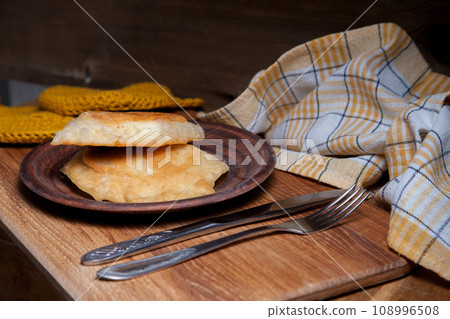 Clay plate of fried meat pies with cutlery on wooden table. Clay plate of fried meat pies with cutlery on wooden table. 108996508